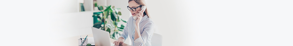 Woman speaks on a phone while looking at computer screen. 